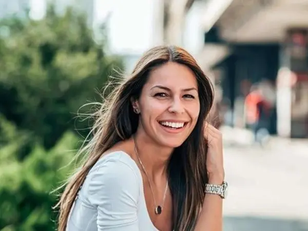 A woman smiling for the camera while wearing a white shirt.