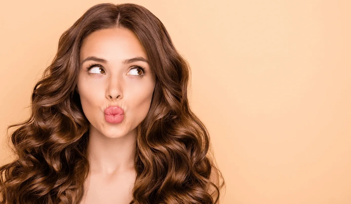 A woman with long brown hair blowing on her lips.