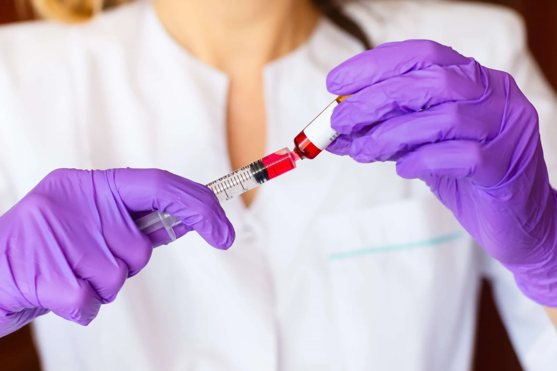 A person in purple gloves holding a syringe.