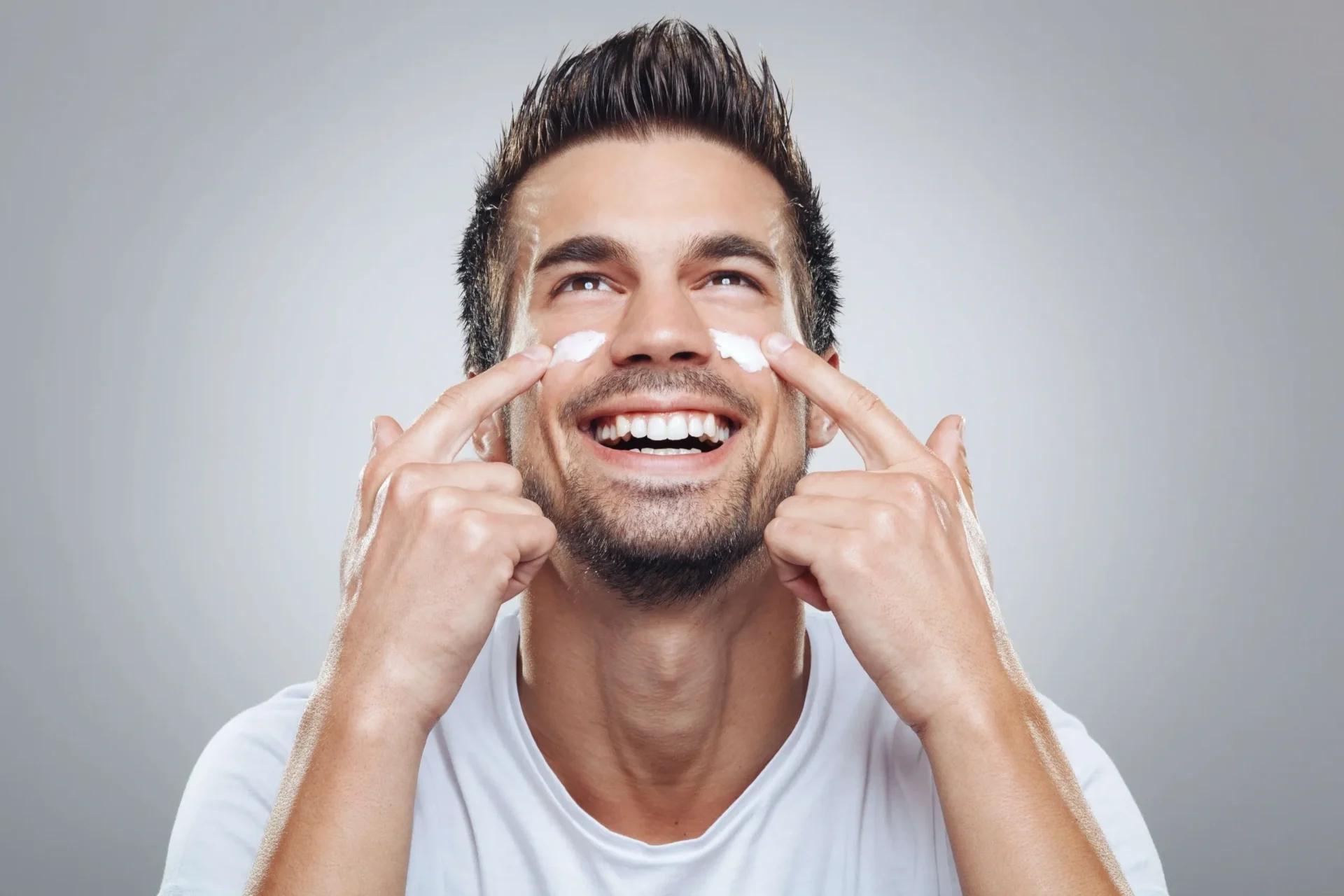 A man putting cream on his face and smiling.