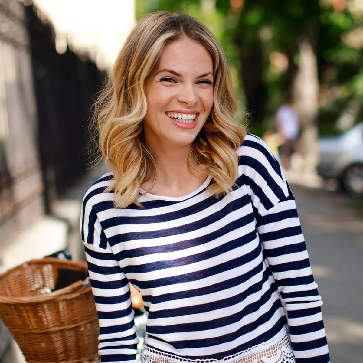 A woman in striped shirt standing on sidewalk next to basket.