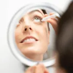 A woman is looking in the mirror while using her makeup.