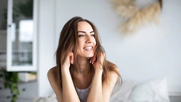 A woman is smiling while holding her hands up to her face.