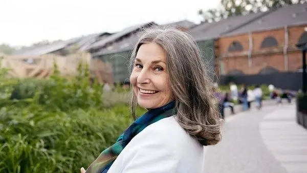 A woman with long grey hair wearing a white jacket.