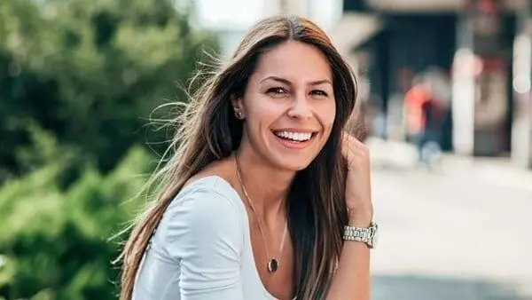 A woman smiling while wearing a white shirt.