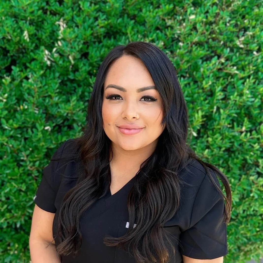 A woman in black shirt standing next to green bushes.