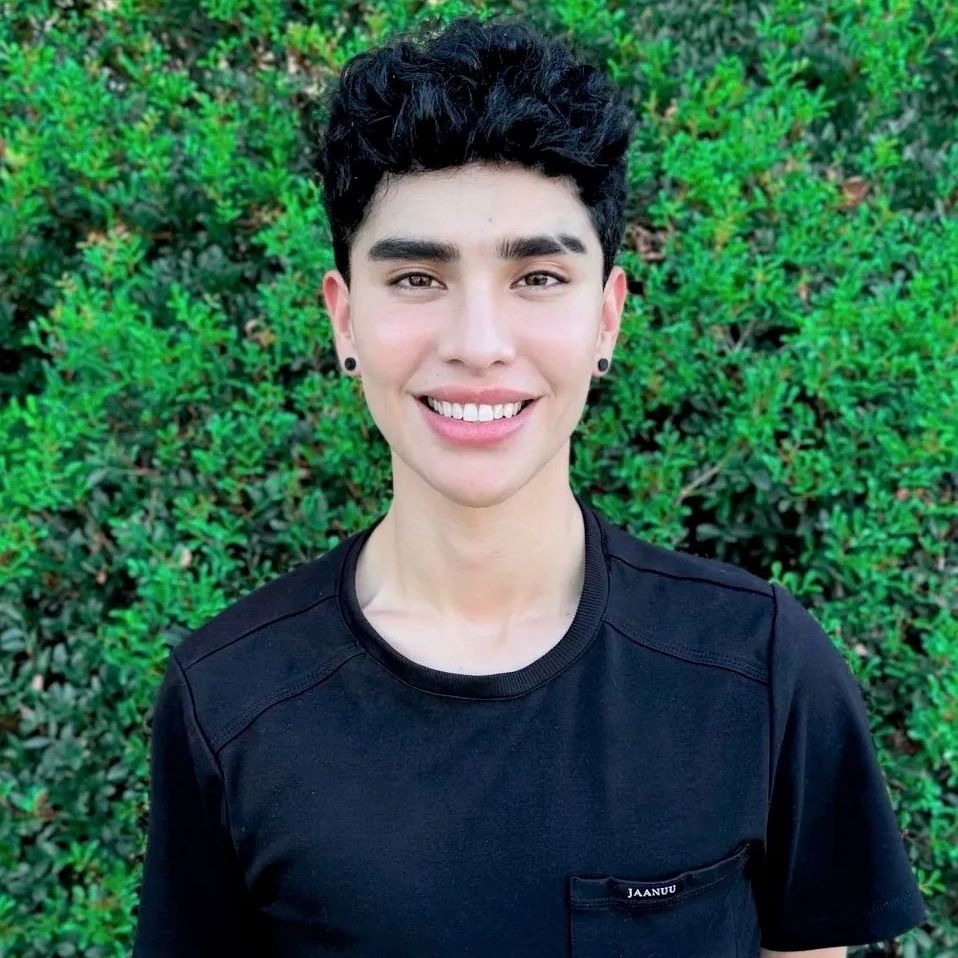 A young man standing in front of bushes.