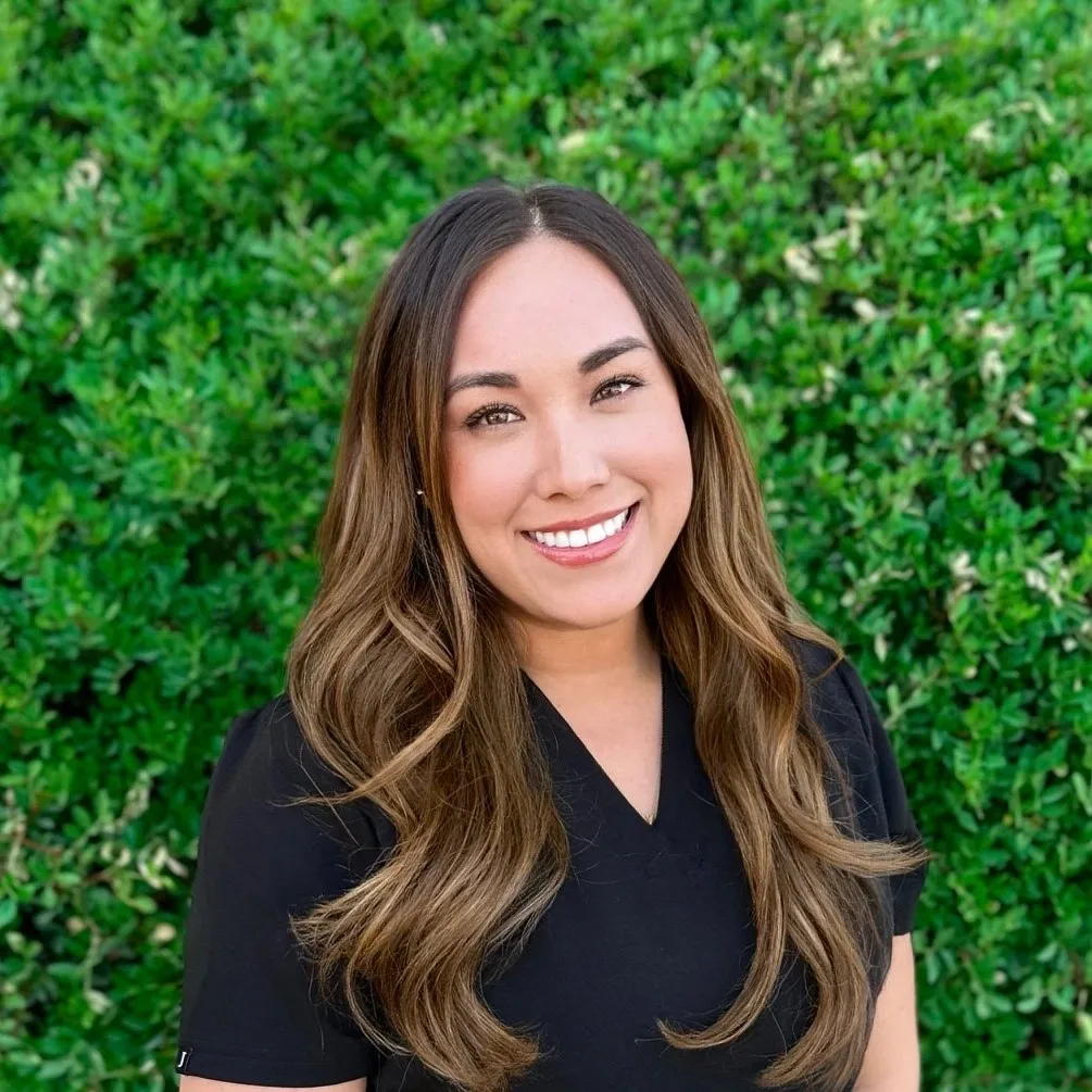 A woman standing in front of a bush smiling.