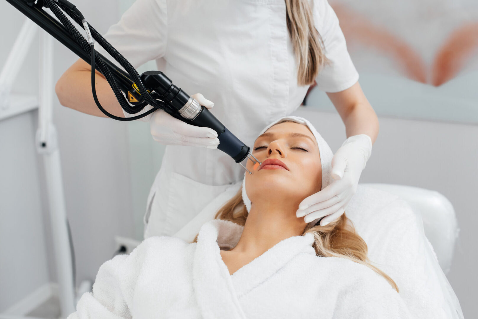 A young girl gets a charcoal peeling for the skin of the face in a beauty salon. Laser pulses cleanse the skin. Hardware cosmetology. The process of photothermolysis, warming the skin.