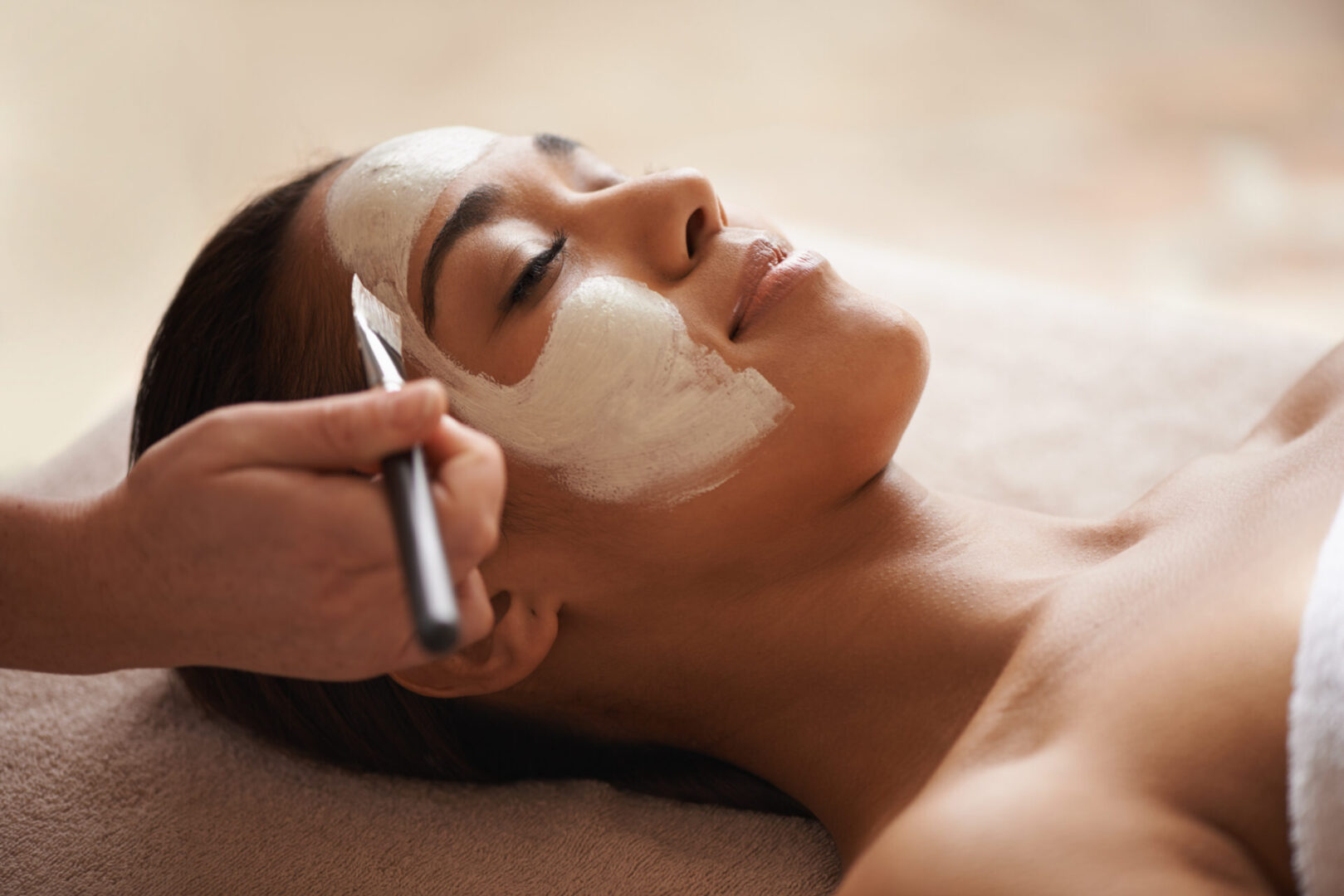 A face mask being applied to a beautiful young woman at a beauty spa.