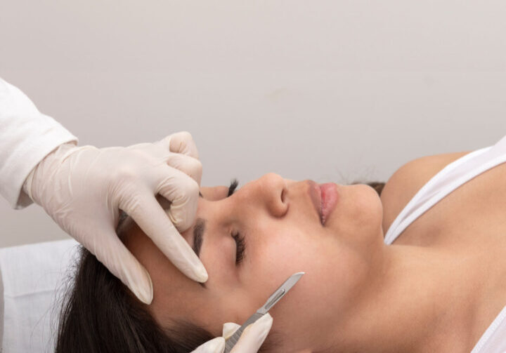 young woman on a table in a beauty center performing a beauty treatment for facial skin with a scalpel using the dermaplaning technique