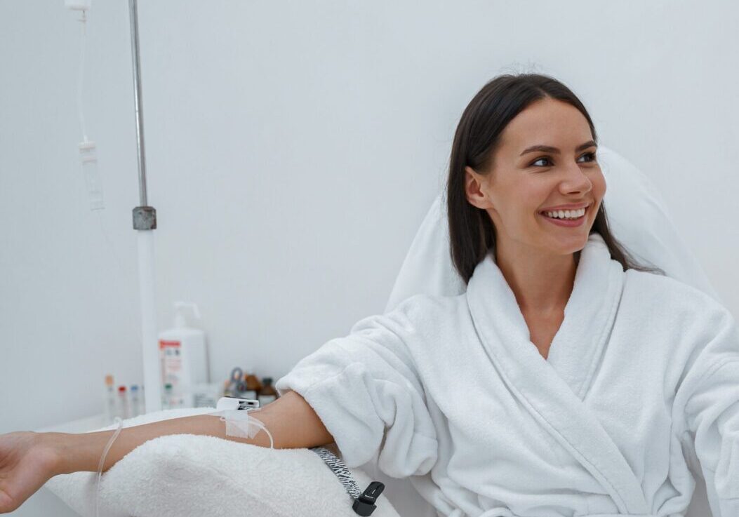 A woman in white robe sitting on chair next to wall.